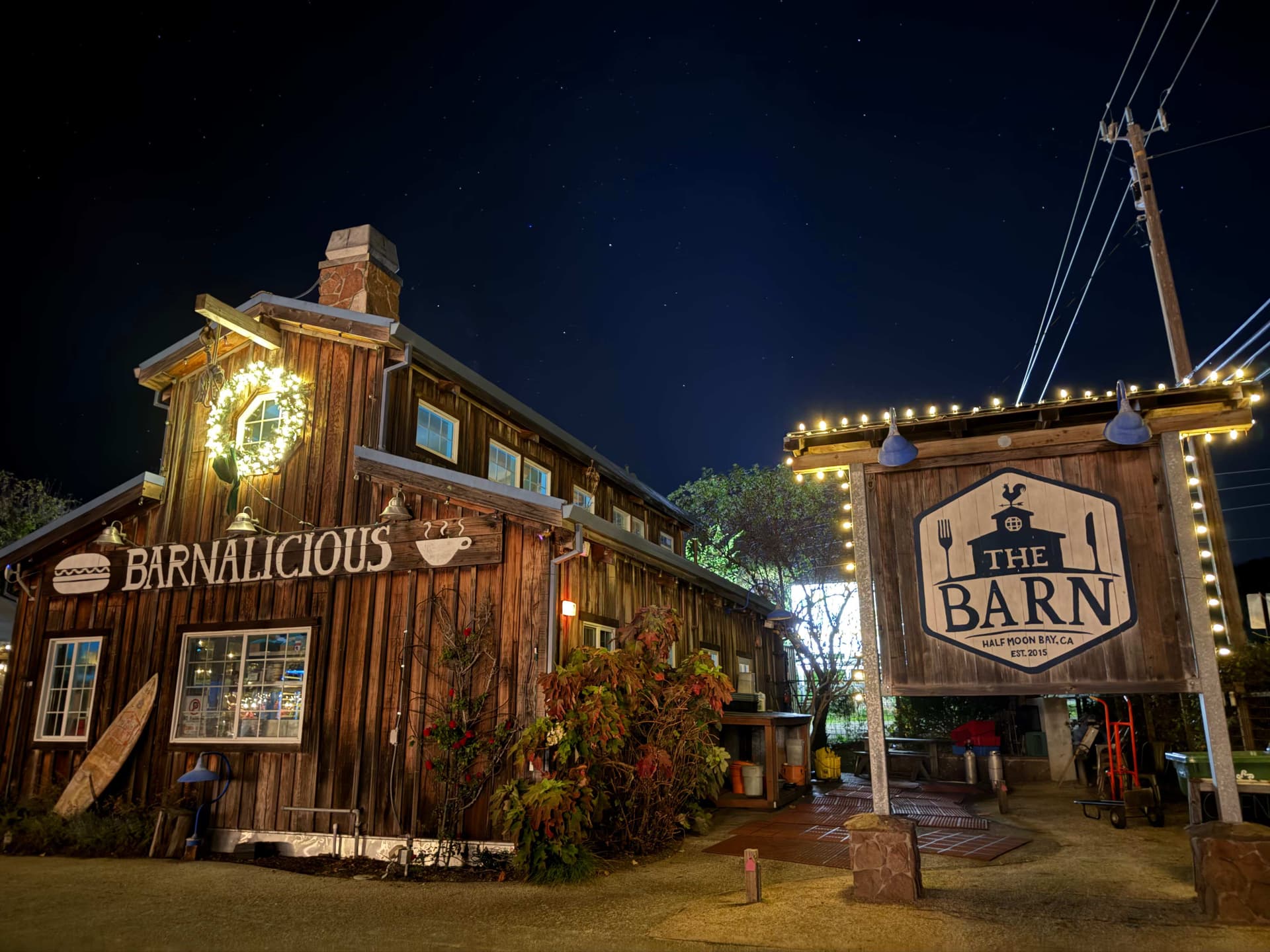 Restaurant entrance at night framed with warm Edison string lights and a lit wreath
