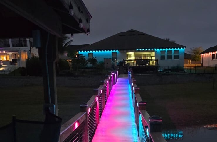 Dock with vibrant RGB lighting leading to homes with smart roofline lighting